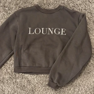 Brun croppad sweatshirt från Lounge - Säljer en brun croppad sweatshirt från Lounge med text på framsidan. Tröjan har långa ärmar och en bekväm passform. Perfekt för en avslappnad stil.