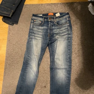 Blå jeans från Jack & Jones - Snygga blå jeans från Jack & Jones med en klassisk femficksdesign och lätt slitna detaljer. De har en bekväm passform och är perfekta för en avslappnad stil. Midjan är normalhög och de har en dragkedja och knapp framtill. Storlek 28/32