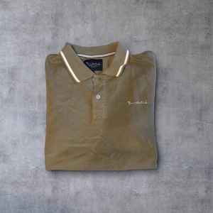 Olivgrön pikétröja från Bondelid - Säljer en stilren olivgrön pikétröja från Bondelid. Tröjan har en klassisk krage med vita detaljer och knappar framtill. Perfekt för en avslappnad men ändå snygg look.