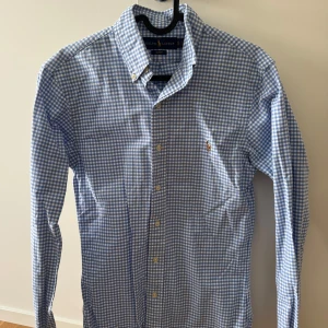 Blåvit rutig skjorta från Ralph Lauren - Säljer en blåvit rutig skjorta från Ralph Lauren i slim fit-modell. Skjortan har klassisk button-down krage, knappar framtill och broderad logga på bröstet. Tillverkad i 100% bomull för en skön känsla.