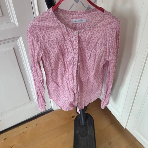 Rosa blommig blus  från Peak Performance - Säljer en söt rosa blus  från Peak Performance med ett blommigt mönster.blus  har långa ärmar och knappar framtill. Perfekt för en avslappnad stil.