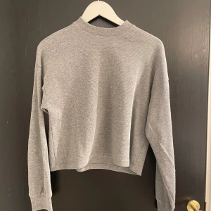 Grå croppad tröja från Zign - Säljer en stilren grå croppad tröja från Zign. Tröjan har en ribbad textur och långa ärmar, perfekt för en avslappnad look. Den är i storlek S och passar bra till både jeans och kjol. Aldrig använd