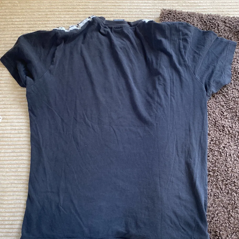 Svart t-shirt från Champion med vit logga på bröstet och loggoband längs axlarna. Klassisk passform och korta ärmar. Perfekt för en sportig och avslappnad stil.. T-paidat.