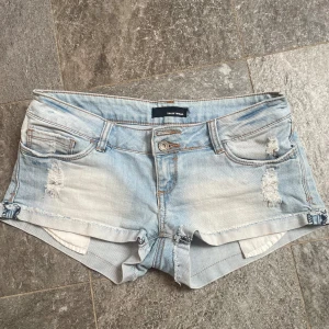Ljusblå jeansshorts med slitningar - Säljer ett par ljusblå jeansshorts från Tally Weijl med slitna detaljer och råa kanter. Shortsen har fem fickor, knapp- och dragkedjestängning samt låg midja. Perfekta för varma dagar! De är verkligen så fina men är tyvärr lite för stora!💗💗