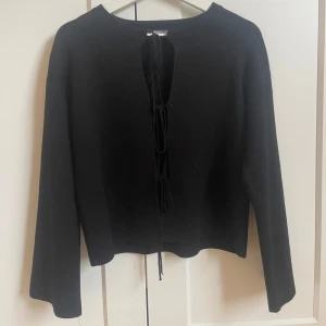Svart tröja med knytning från Gina Tricot - Svart långärmad tröja från Gina Tricot med snygg knytning framtill. Tröjan har en rak passform och är tillverkad i ett mjukt material. Perfekt för dig som gillar stilrena plagg med en twist. Använt 1 gång så är precis som ny💗