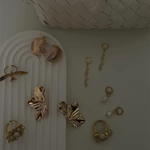 Mix av guldiga örhängen med pärldetaljer - Säljer flera olika guldiga örhängen, bland annat stora blommiga och fjärilsformade modeller, hoops, samt örhängen med pärlor och gnistrande detaljer. Perfekt för dig som vill variera din stil med unika accessoarer.