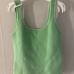 Grön ribbad linnetopp - Snygg grön ribbad linnetopp med breda axelband och rundad halsringning. Perfekt för varma dagar och enkel att matcha med jeans eller kjol.