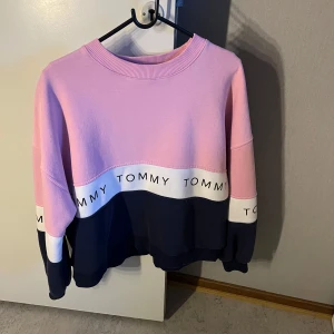 Rosa och marinblå sweatshirt från Tommy Jeans - Säljer en snygg sweatshirt från Tommy Jeans i rosa och marinblått med vit rand och logga runt hela tröjan. Tröjan har rund halsringning och långa ärmar. Perfekt för en avslappnad stil.