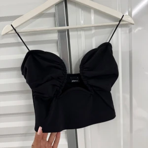 Svart croppad linnetopp med tunna axelband - Oanvänd Trendig svart croppad linnetopp från Shein med tunna axelband och rynkade kupor. Toppen har en snygg passform och dragkedja bak för enkel på- och avtagning. Perfekt för att skapa en cool och stilren look.