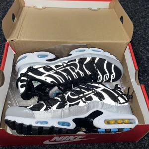 Nike Air Max Plus TN svart och vit - Säljer ett par Nike Air Max Plus TN i svart och vit med reflekterande detaljer och blå inslag i sulan. Skorna har snörning, synlig Air Max-dämpning och ett unikt mönster på ovandelen. 