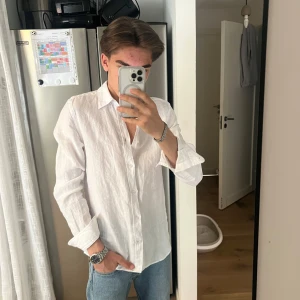 Vit linneskjorta från J.Lindeberg - Säljer en stilren vit skjorta i linne från J.Lindeberg. Skjortan har klassisk krage, knäppning framtill och långa ärmar. Perfekt för en fräsch och avslappnad look. Passar dig som gillar en normal passform och vill ha något svalt och luftigt.