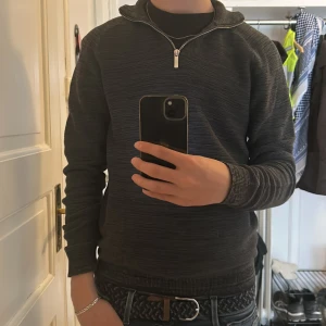 Mörkgrå tröja med dragkedja från Primark - Säljer en mörkgrå tröja från Primark med halv dragkedja vid halsen. Tröjan har lång ärm och en diskret, melerad struktur. Perfekt för en avslappnad och stilren look.