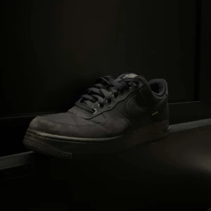 Mörkblå Nike Air Force  - Snygga mörkblå Nike Air Force med material för extra hållbarhet och väderskydd. Skorna har en klassisk design med snörning och en robust sula. Perfekta för både stil och funktion. Liten defekt på höger skon.