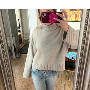 Beige stickad polotröja - Säljer en mysig beige stickad polotröja med ribbade detaljer vid ärmslut och nederkant. Tröjan har en avslappnad passform och långa ärmar, perfekt för kyligare dagar. 