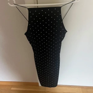 Svart prickig tight klänning med tunna axelband - Säljer en svart tight klänning med tunna axelband och vita prickar. Klänningen har en kroppsnära passform och är perfekt för dig som gillar en stilren look med lite edge. Passar till många olika tillfällen!
