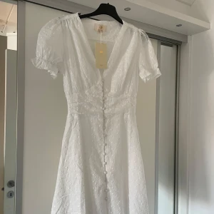 Vit sommar klänning - Säljer en söt vit klänning från Chelsea i storlek XS, aldrig använd och har lappen kvar. Klänningen har korta puffärmar, v-ringning och knappar framtill. Perfekt för sommaren, student, skolavslutning eller konfirmation❤️❤️