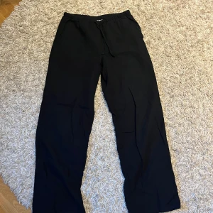 Svarta linnebyxor  från Gina Tricot - Svarta linnebyxor från Gina Tricot med resår i midjan och dragsko. Byxorna har en rak och avslappnad passform, perfekta för en chill vardagslook. Tillverkade i ett mjukt och lätt material som känns skönt mot huden.