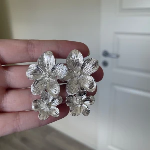 Silvriga blommiga örhängen - Snygga silvriga örhängen i form av blommor. De har en vacker, detaljerad design med flera lager av blomblad som ger en elegant look. Perfekta för att ge en extra touch till din outfit.