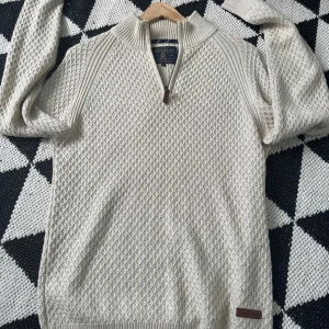 Beige stickad tröja från Bondelid - Säljer en snygg beige stickad tröja från Bondelid med dragkedja vid halsen. Tröjan har ett diskret mönster och ribbade detaljer vid ärmslut och nederkant. Perfekt för sena sommar kvällar!