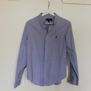 Blå skjorta från Ralph Lauren - Snygg blå skjorta från Ralph Lauren med klassisk krage och broderad logotyp på bröstet. Skjortan har långa ärmar och knappar framtill. Perfekt för en stilren look.