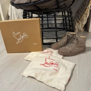 Christian Louboutin sneakers  - Säljer ett par sneakers från Christian Louboutin med coola nitar över hela skon. De har snörning och den klassiska röda sulan som märket är känt för. Perfekta för att ge din outfit en edgy touch.