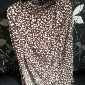 Brun blommig långkjol  - Säljer en brun långkjol med vitt blommönster. Kjolen har en lös passform och är perfekt för varmare dagar. Den är lång och har ett mjukt, följsamt tyg som ger en avslappnad känsla.