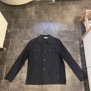 Overshirt - Snygg mörkblå overshirt från sandö som är helt ny och aldrig använd. Säljs pågrund av att den aldrig kom till användning. Nypris ligger på 1300kr.