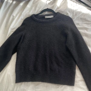 Svart stickad tröja från Carin Wester - Säljer en stilren svart stickad tröja från Carin Wester. Tröjan har en klassisk design med rund hals och långa ärmar, perfekt för kyligare dagar. Den är mjuk och bekväm, idealisk för både vardag och mer avslappnade tillfällen.