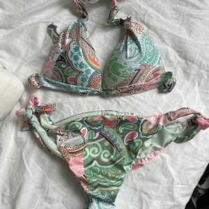 Mönstrad bikini från Calzedonia - Säljer en snygg bikini från Calzedonia med paisleymönster i grönt, rosa och turkost. Både överdel och underdel har knytband i sidorna och nacken. Perfekt för stranden eller poolen! Aldrig använd!💕