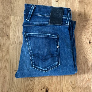 Replay Anbass blå jeans - Snygga Replay Anbass jeans i klassisk blå tvätt med lätt slitning och raka ben. Jeansen har fem fickor, normal passform och tydliga Replay-detaljer på bakfickan och myntfickan. Perfekta för en avslappnad och stilren look. Storlek 30/34, den är i ett mycket bra skick. Hör av er vid frågor!😊