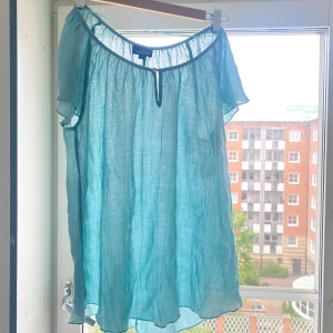 Turkos blus i linne från KappAhl - Luftig turkos blus från KappAhl i linne. Modellen har korta ärmar, rundad halsringning med liten knappdetalj framtill och en lätt transparent känsla. Perfekt för varma dagar när du vill ha något svalt och stilrent.