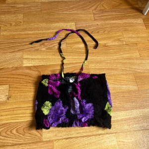 Svart bandeau tubtopp med blommor - En cool bandeau tubtopp med smock och halterneck. Toppen är svart med stora blommiga mönster. Fin till sommaren. 