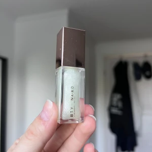 Skimrigt läppglans - Glansigt läppglans från BTY by NA-KD i färgen Clear med skimrande effekt. Kommer i en stilren fyrkantig flaska med roséguldfärgat lock. Vegansk formula och innehåller 5,5 g. Perfekt för att ge läpparna en glittrig finish.