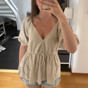 Beige blus med knytning - Superfin beige blus från BikBok i luftig linnemix. Den går att både klä upp och klä ner. Det är ett perfekt sommarplagg som både är snyggt och skönt. Den är i storlek xs men den är ganska stor i storleken och som sagt väldigt luftig.🌼💛💛 (Jag har satt ett gem för att göra urringningen mindre, detta går såklart att ta bort men om man vill ha med gemet vid köpet så går det också superbra!)