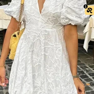 Vit kortklänning med puffärm - Superfin vit kortklänning med broderade blommönster och puffiga korta ärmar. Klänningen har v-ringning och markerad midja som ger en snygg siluett. Perfekt för sommarens alla tillfällen och ger en romantisk vibe. 
