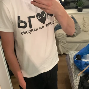 Vit Comme des Garçons Play t-shirt - Vit-shirt med svart tryck och det ikoniska hjärtögat från Comme des Garçons play på bröstet. Klassisk rund hals och korta ärmar. Perfekt för en clean och stilren look.   Vid funderingar eller annat kring tröjan tveka då inte att höra av dig!!