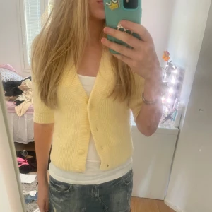 Gul stickad kofta från Monki - Säljer en söt ljusgul stickad kofta från Monki i storlek XS. Koftan har korta ärmar, v-ringning och knappar framtill. Perfekt att ha öppen eller stängd över ett linne eller t-shirt. Supermjuk och mysig känsla!