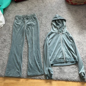 Grå velourbyxor och en zip hoodie från Gina Tricot  - Mysiga grå velourbyxor från Gina Tricot med bootcut-snitt och dragsko i midjan. Byxorna har bakfickor och är perfekta för en chill och avslappnad stil. Matchar snyggt med hoodie i samma material för en komplett look. Tröjan är ganska liten i storlek.