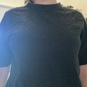 Svart basic t-shirt från 157 - Enkel svart t-shirt från 157 med rund hals och rak passform. T-shirten är kortärmad och gjord i mjuk bomull, perfekt för en clean och avslappnad stil. Passar till allt och är ett måste i garderoben.