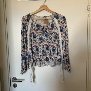 Odd molly poncho/blus  - Troligt vacker poncho blus som har en creme färgad bottenfärg med blommiga detaljer i färgerna blått och rosa. Finns även spetisband på både fram och baksidan av toppen. Toppen har även små medvetna ”hål”. Knappar längst ärmarna. Från märket Odd Molly i storlek 1 som ungefär motsvarar en Storlek S. kanske kan vara något rymlig i storlek. Mycket fint skick, jag hittar inga synlig anmärkningar eller defekter. 