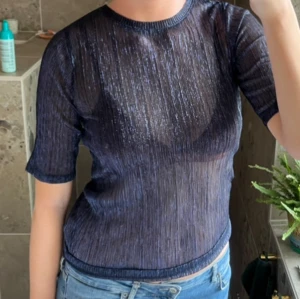 Glittrig mörkblå mesh topp - Säljer en glittrig mörkblå mesh topp med korta ärmar och rund hals. Tunt, transparent material med glitter. Perfekt fest topp