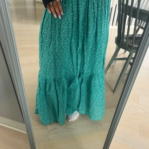 Grön mönstrad långkjol med volang - Säljer en grön långkjol med snyggt geometriskt mönster och bred resår i midjan. Kjolen har volang nertill som ger extra flow och en chill vibe. Perfekt för dig som vill ha något bekvämt men ändå trendigt.