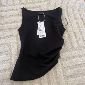 Svart ärmlös topp från Gina Tricot - Säljer en svart, stilren ärmlös topp från Gina Tricot. Toppen har en enkel och clean design med rund halsringning och figurnära passform. Perfekt att matcha med jeans eller kjol för en snygg look.