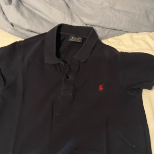 Svart pikétröja från Polo Ralph Lauren - Klassisk svart pikétröja från Polo Ralph Lauren med röd broderad logga på bröstet. 