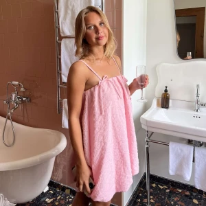 Ljusrosa kort klänning med rosett - Supersöt ljusrosa kort klänning med tunna axelband och en liten rosett framtill. Klänningen har en luftig och lös passform, perfekt för varma dagar. Materialet är mjukt och har en lätt struktur som ger en chill vibe.