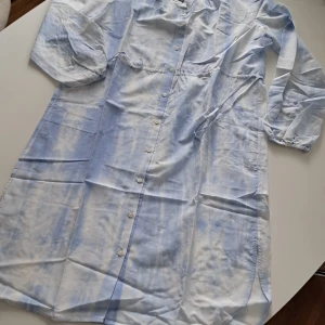 Blåvit tie dye klänning Marc O'Polo - Superfin långklänning från Marc O'Polo i blåvitt tie dye-mönster. Klänningen har knappar hela vägen framtill, långa ärmar med resår vid handlederna och knyt i midjan. Materialet är en lyxig mix av bomull och silke som känns lätt och sval. Obs! Passar även som storleken "M" (mått: L 103 cm, Axlarna ca. 41,5 cm)