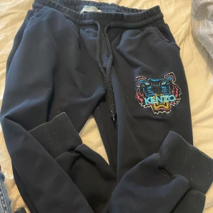 Svarta mjukisbyxor Kenzo XL - Svarta mjukisbyxor från Kenzo i storlek XL, men det passar en person som har XXS och XS. Broderad tigerlogga i färg på ena benet. Byxorna har resår i midjan, snörning och muddar vid bensluten. Perfekta för en chill och trendig look. Pris kan diskuteras