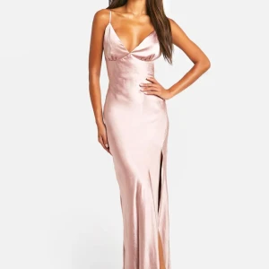 Ljusrosa långklänning i satin - Supersnygg långklänning i ljusrosa satin med smala axelband, v-ringning och en hög slits framtill. Klänningen har en figurnära passform och glansigt material som ger en lyxig känsla. Helt oanvänd med prislapp kvar.