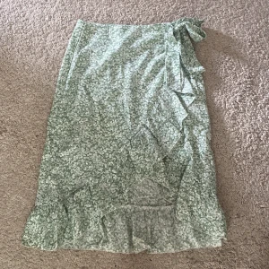 Grön blommig omlottkjol med volang - Söt grön omlottkjol med vitt blommönster och volangkant.