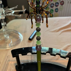 Unikt spindel-penna med pärlor - Coolt penna med en stor spindel i brunt och svart på toppen, dekorerat med gröna, svarta och lila pärlor samt glittrande detaljer. Kedjan är grön och designen är riktigt iögonfallande och edgy – perfekt för dig som vill sticka ut.
